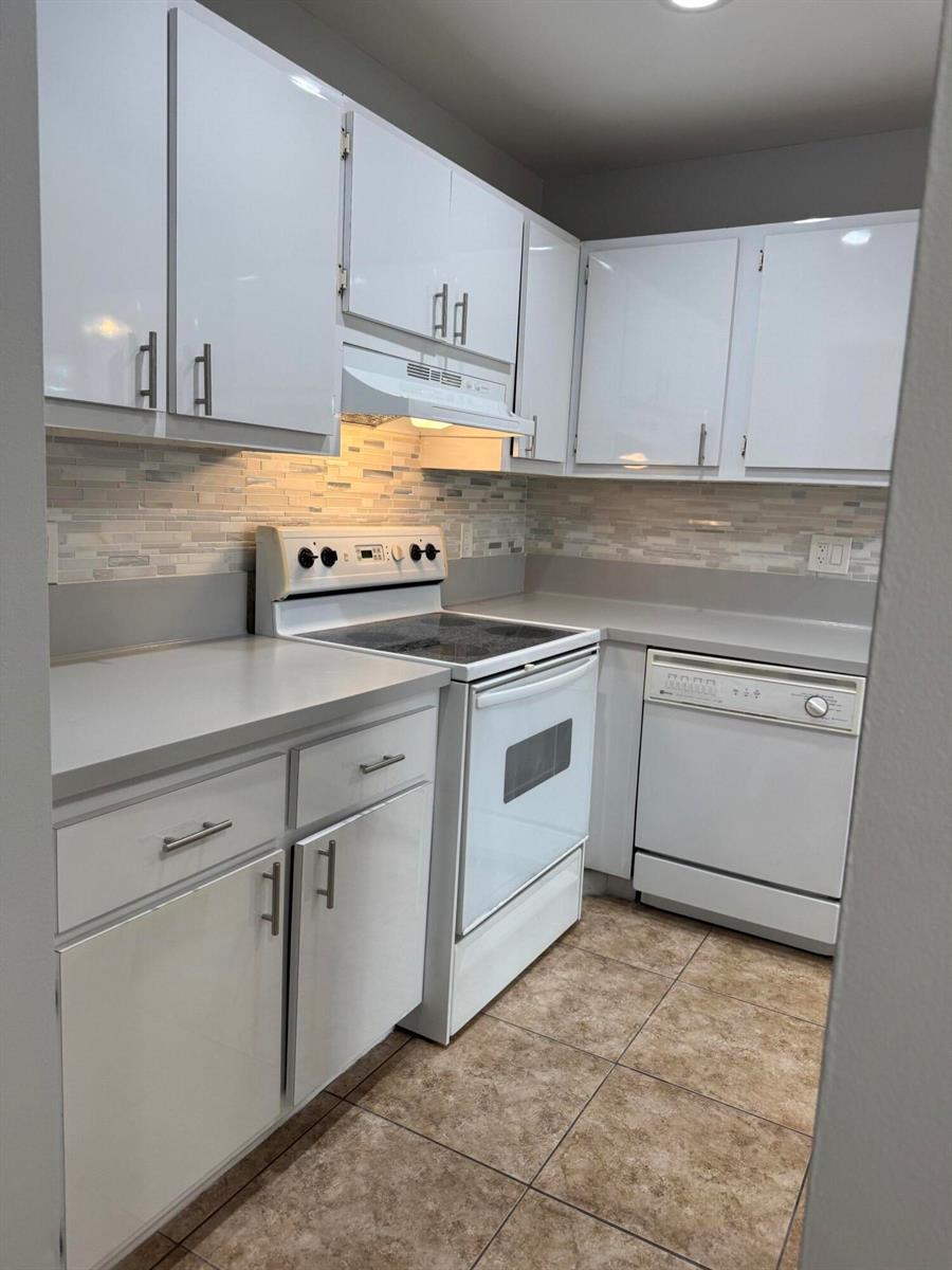 A kitchen features white cabinets, light countertops, a tiled backsplash, and white appliances — 1100 Boxwood Drive # 101, Delray Beach FL 33445, DELRAY BEACH, FL