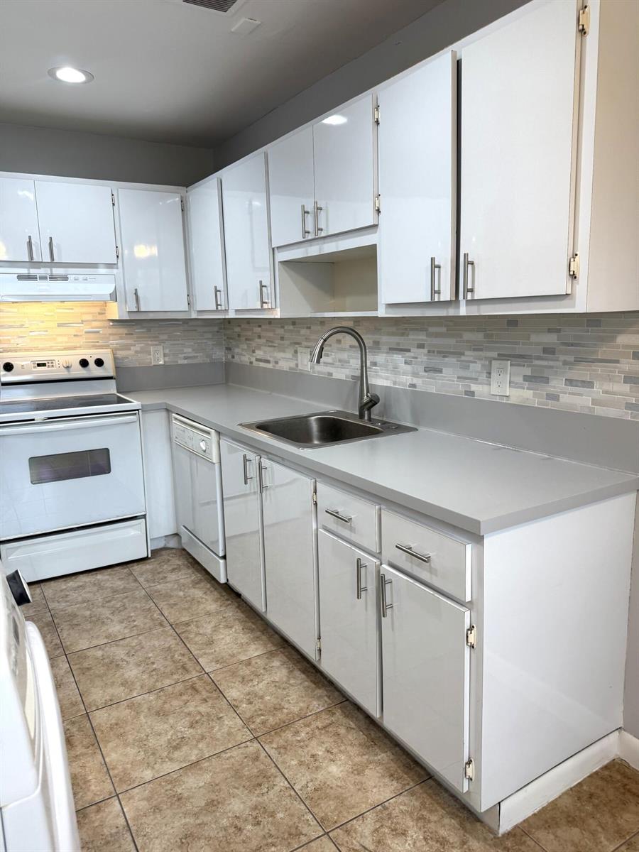A kitchen features white cabinets, gray countertops, a stainless steel sink, and tiled flooring — 1100 Boxwood Drive # 101, Delray Beach FL 33445, DELRAY BEACH, FL