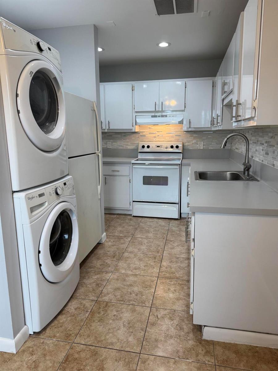 A galley kitchen features white cabinets, a stacked washer and dryer, and tile flooring — 1100 Boxwood Drive # 101, Delray Beach FL 33445, DELRAY BEACH, FL