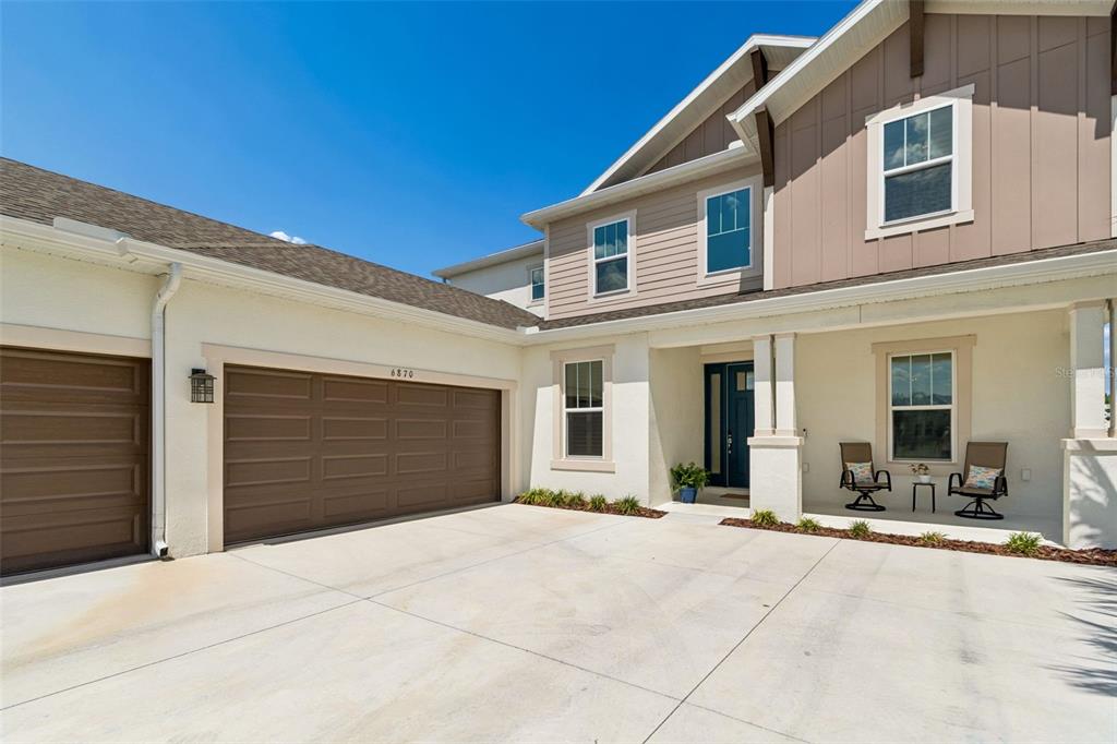 A two-story house exterior features a tan stucco facade, a brown garage, and a front porch — 6870 TALAMORE DRIVE, WESLEY CHAPEL, FL