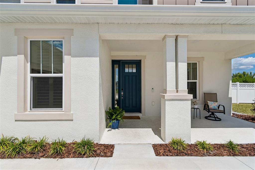 A front porch with a blue door, a window, and a chair on a concrete slab — 6870 TALAMORE DRIVE, WESLEY CHAPEL, FL
