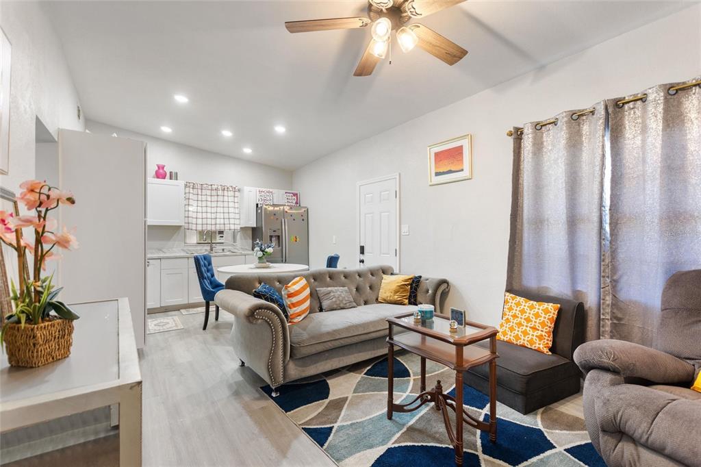 A living room and kitchen area feature light wood flooring, a grey sofa, and rugs — 1495 PENNIWA STREET, INTERCESSION CITY, FL