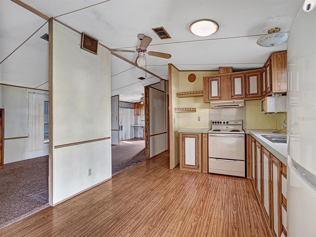 A kitchen with wood-look flooring, wood cabinets, and an off-white stove opens to carpeted rooms — 10339 MARINETTE AVENUE, HUDSON, FL