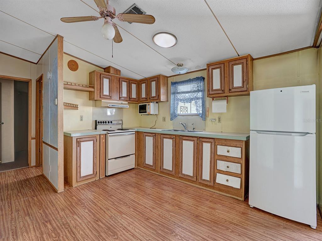 A kitchen features wood-trimmed cabinets, white appliances, and wood-look flooring under a ceiling fan — 10339 MARINETTE AVENUE, HUDSON, FL