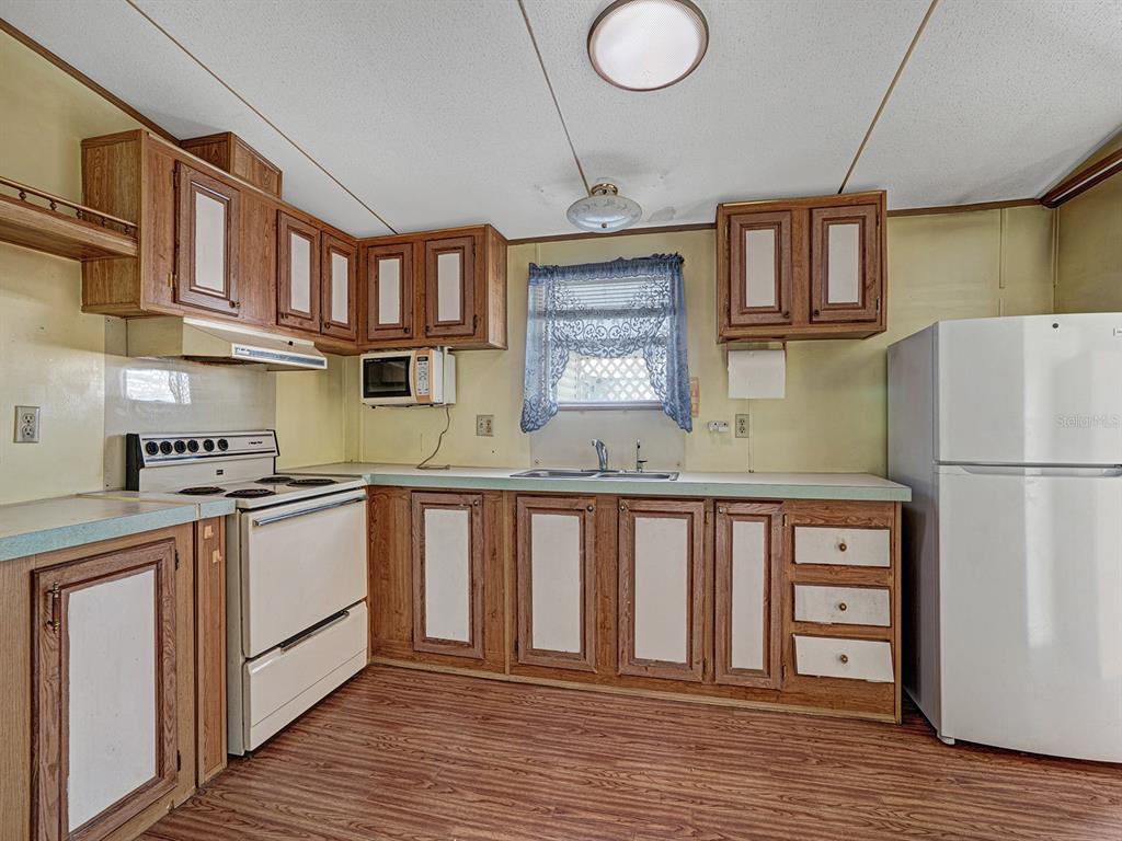A kitchen features wood-trimmed cabinets, a white stove, a refrigerator, and wood-look flooring — 10339 MARINETTE AVENUE, HUDSON, FL