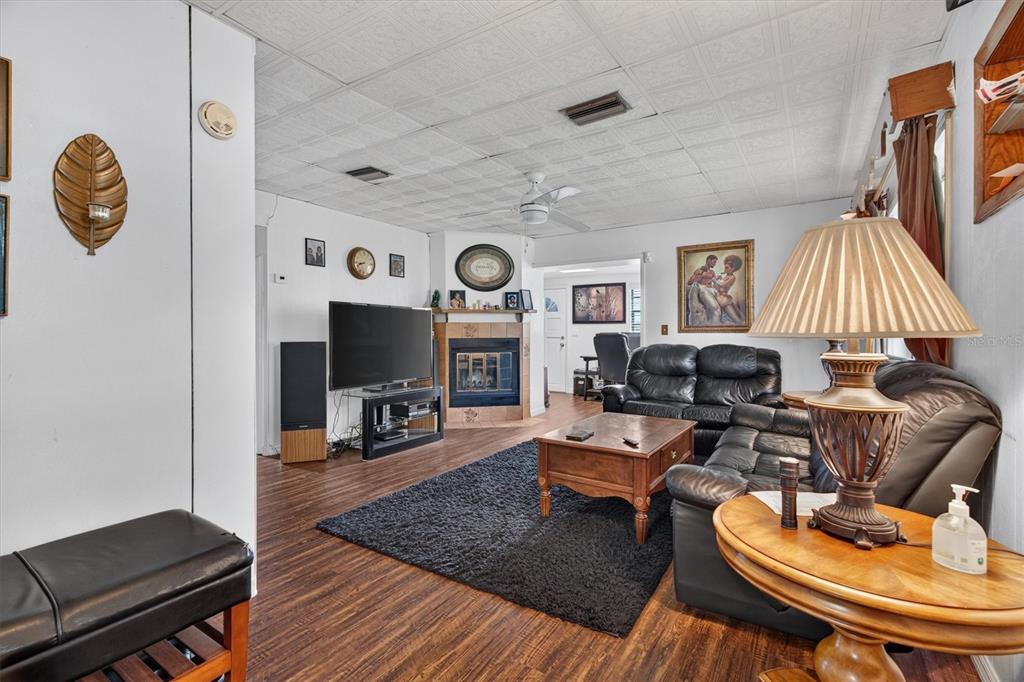A living room features a fireplace, black leather furniture, wood flooring, and a drop ceiling — 1865 CEDARWOOD DRIVE, MELBOURNE, FL