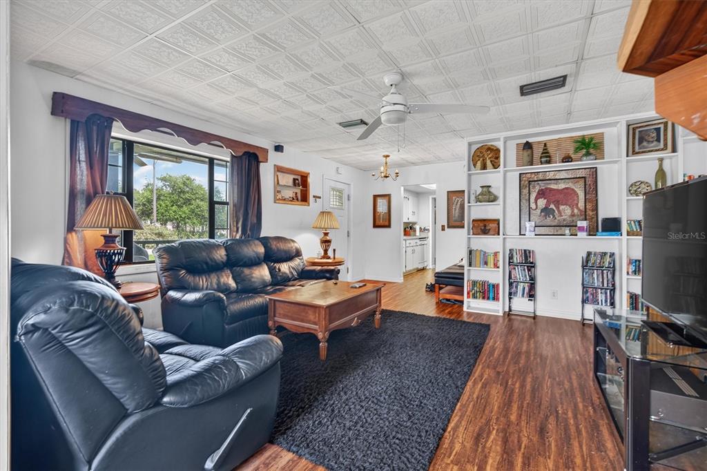 A living room features a black leather sofa, wood flooring, a ceiling fan, and built-in shelving — 1865 CEDARWOOD DRIVE, MELBOURNE, FL