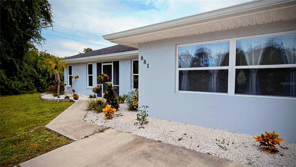 A light blue house exterior features a concrete walkway, white gravel landscaping, and large windows — 881 BAYSHORE DRIVE, ENGLEWOOD, FL