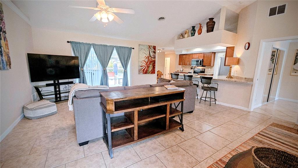 A living room with tile floors features a sofa, television, and an open kitchen area — 881 BAYSHORE DRIVE, ENGLEWOOD, FL