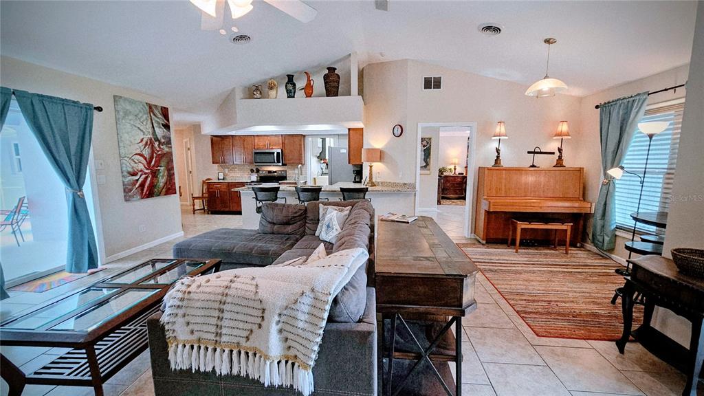 A living room with a sectional sofa, piano, and an open kitchen with wooden cabinets — 881 BAYSHORE DRIVE, ENGLEWOOD, FL