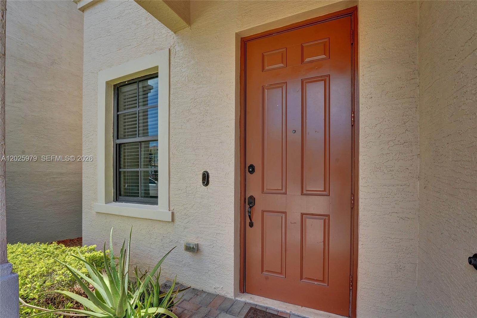 A brown front door is set in a beige stucco wall next to a window — 650 NE 191st Ter, Miami FL 33179, MIAMI, FL