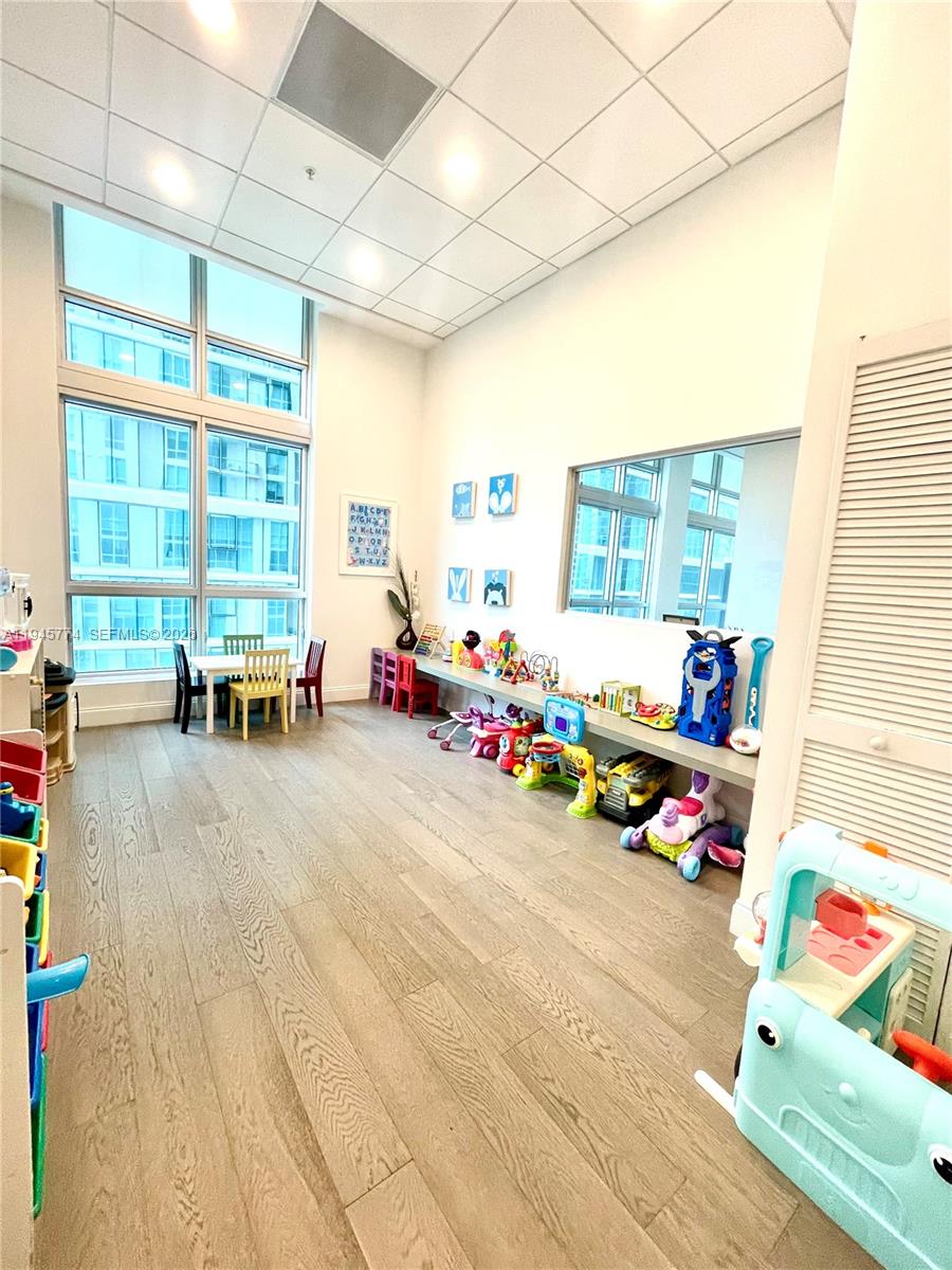 A brightly lit children's playroom features tall windows, wood-look flooring, and a long storage shelf — 300 S Biscayne Blvd # 1803, Miami FL 33131, MIAMI, FL