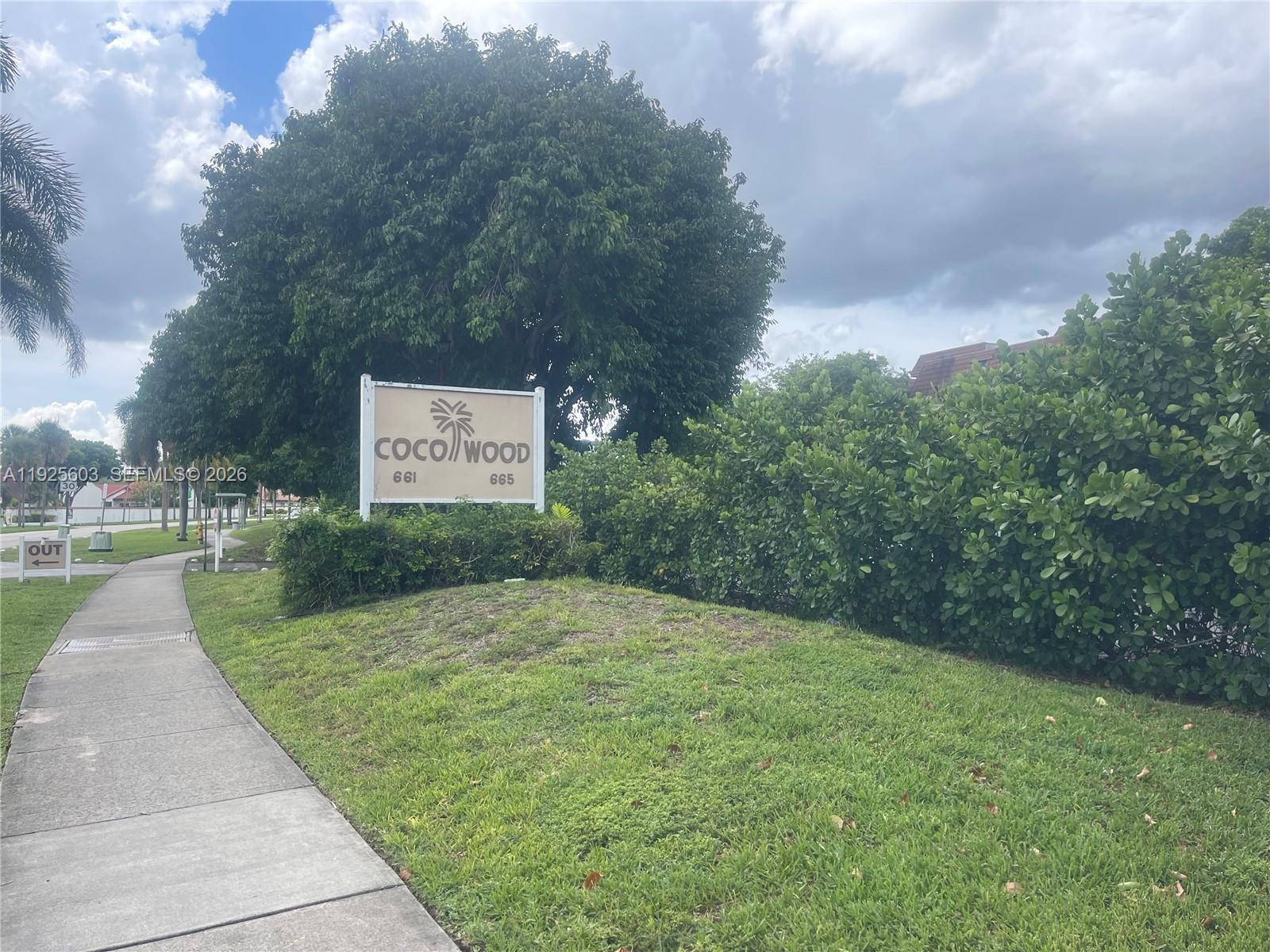 A sign for Coco Wood stands on a grassy lawn next to a concrete sidewalk — 661 NE 195th St # 309, Miami FL 33179, MIAMI, FL