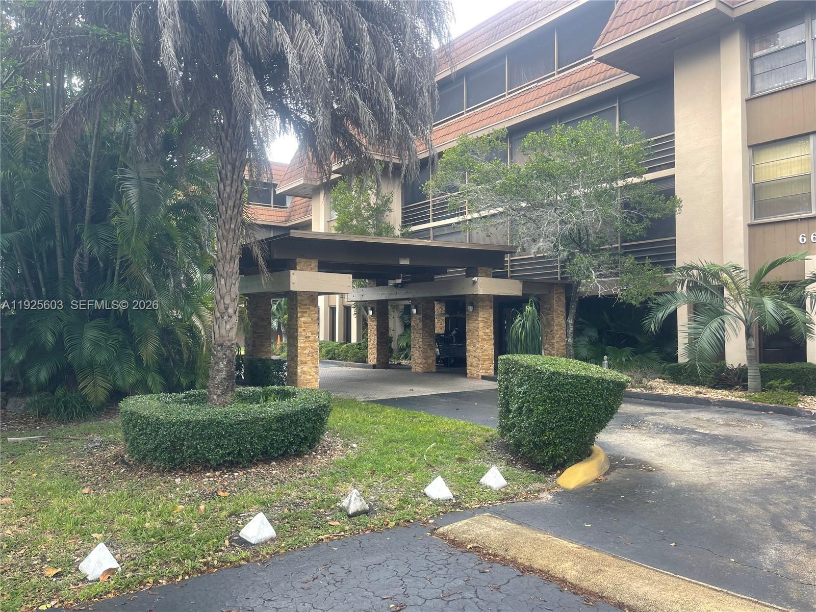 A multi-story building features a covered entrance with stone pillars and surrounding landscaping — 661 NE 195th St # 309, Miami FL 33179, MIAMI, FL