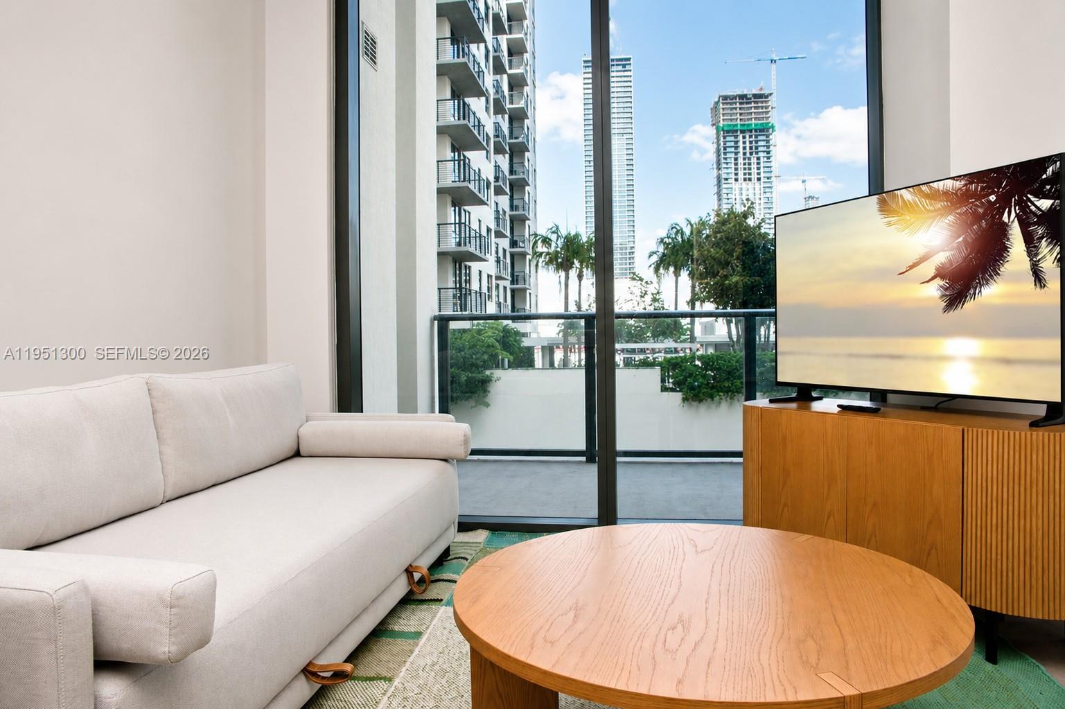 A living room features a light-colored sofa, a round wooden coffee table, and a television — 11 NE 6th St # 1109, Miami FL 33132, MIAMI, FL