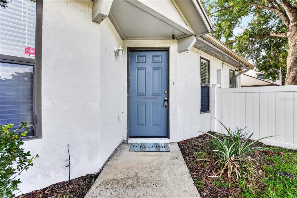 A blue front door with a welcome mat stands under a covered entryway — 1214 CREEKBOTTOM CIRCLE, ORLANDO, FL
