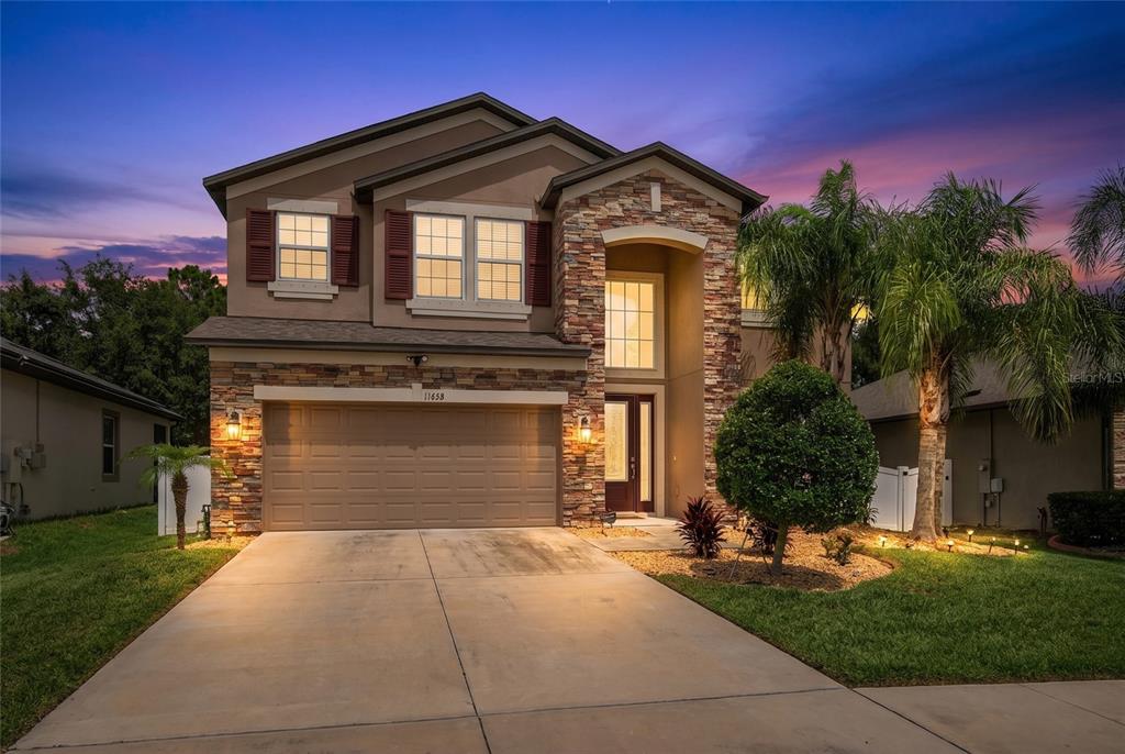 A two-story suburban house with a stone facade, a two-car garage, and a concrete driveway — 11438 ACACIA GROVE LANE, RIVERVIEW, FL