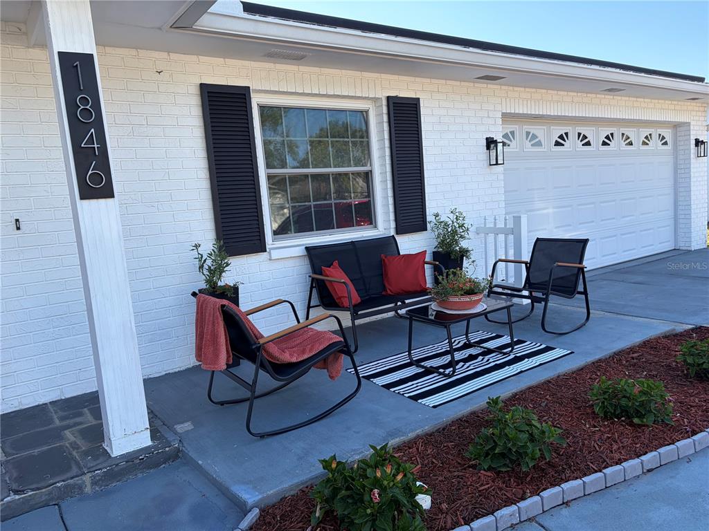 A white brick house exterior features a front patio with black furniture and a rug — 1846 ELMHURST DRIVE, CLEARWATER, FL