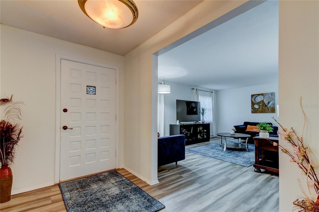 An entryway with a white front door leads into a living room with wood-look flooring — 1846 ELMHURST DRIVE, CLEARWATER, FL