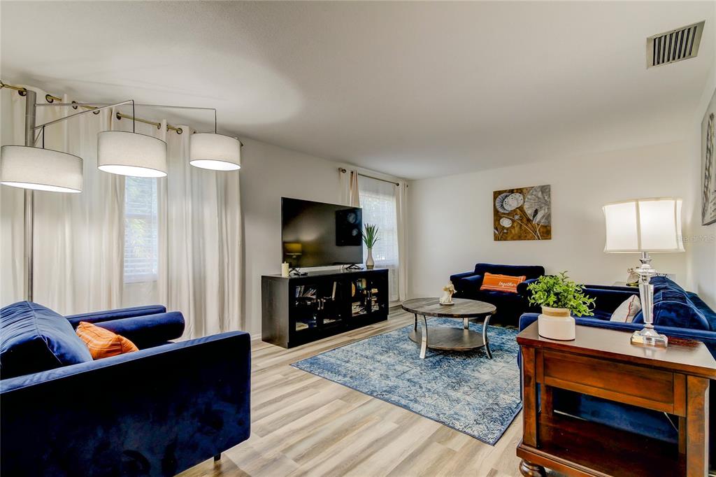 A living room features blue velvet sofas, a television on a console, and wood-look flooring — 1846 ELMHURST DRIVE, CLEARWATER, FL