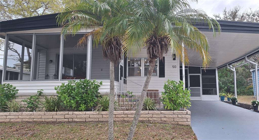 A single-story manufactured home with a screened porch, carport, and palm trees in the front — 50 DOGWOOD COURT UNIT 11, SAFETY HARBOR, FL