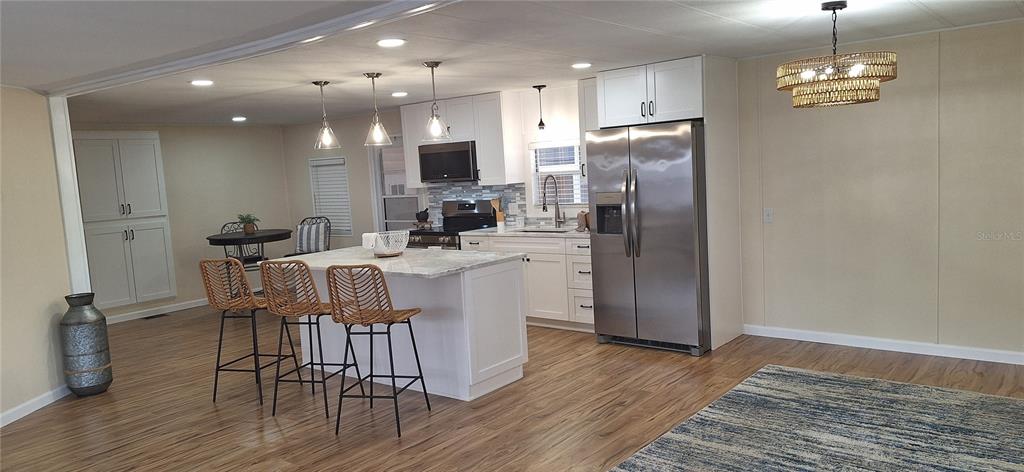 A kitchen features a white island with bar stools, stainless steel appliances, and wood flooring — 50 DOGWOOD COURT UNIT 11, SAFETY HARBOR, FL