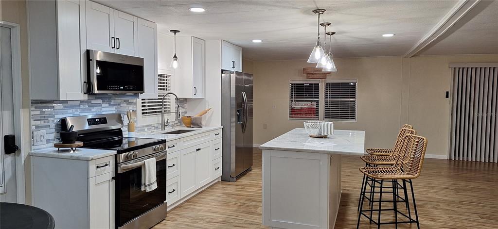 A modern kitchen features white cabinetry, stainless steel appliances, and a marble-topped island with stools — 50 DOGWOOD COURT UNIT 11, SAFETY HARBOR, FL