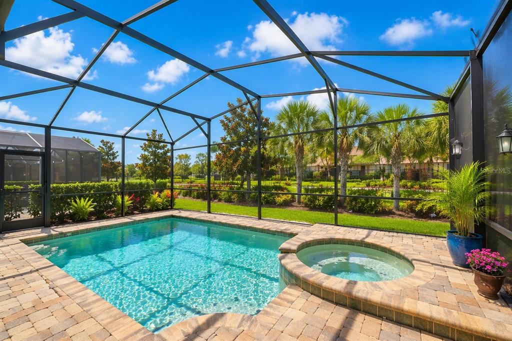 A screened-in pool and spa area with stone pavers and a view of palm trees — 8951 AMELIA DOWNS TRAIL, KISSIMMEE, FL