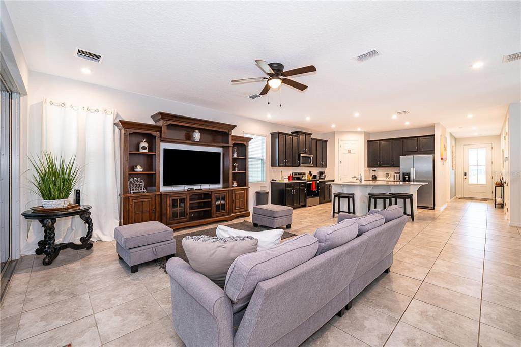 An open-concept living room and kitchen featuring tile floors, dark cabinetry, and a ceiling fan — 8951 AMELIA DOWNS TRAIL, KISSIMMEE, FL