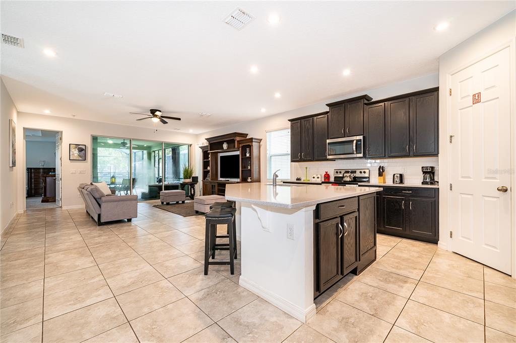 An open-concept kitchen and living area features dark cabinetry, a central island, and tile flooring — 8951 AMELIA DOWNS TRAIL, KISSIMMEE, FL