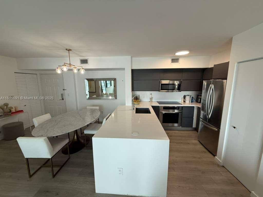 A modern kitchen features a white island, dark cabinetry, stainless steel appliances, and an adjacent dining area — 1155 Brickell Bay Dr # 1408, Miami FL 33131, MIAMI, FL