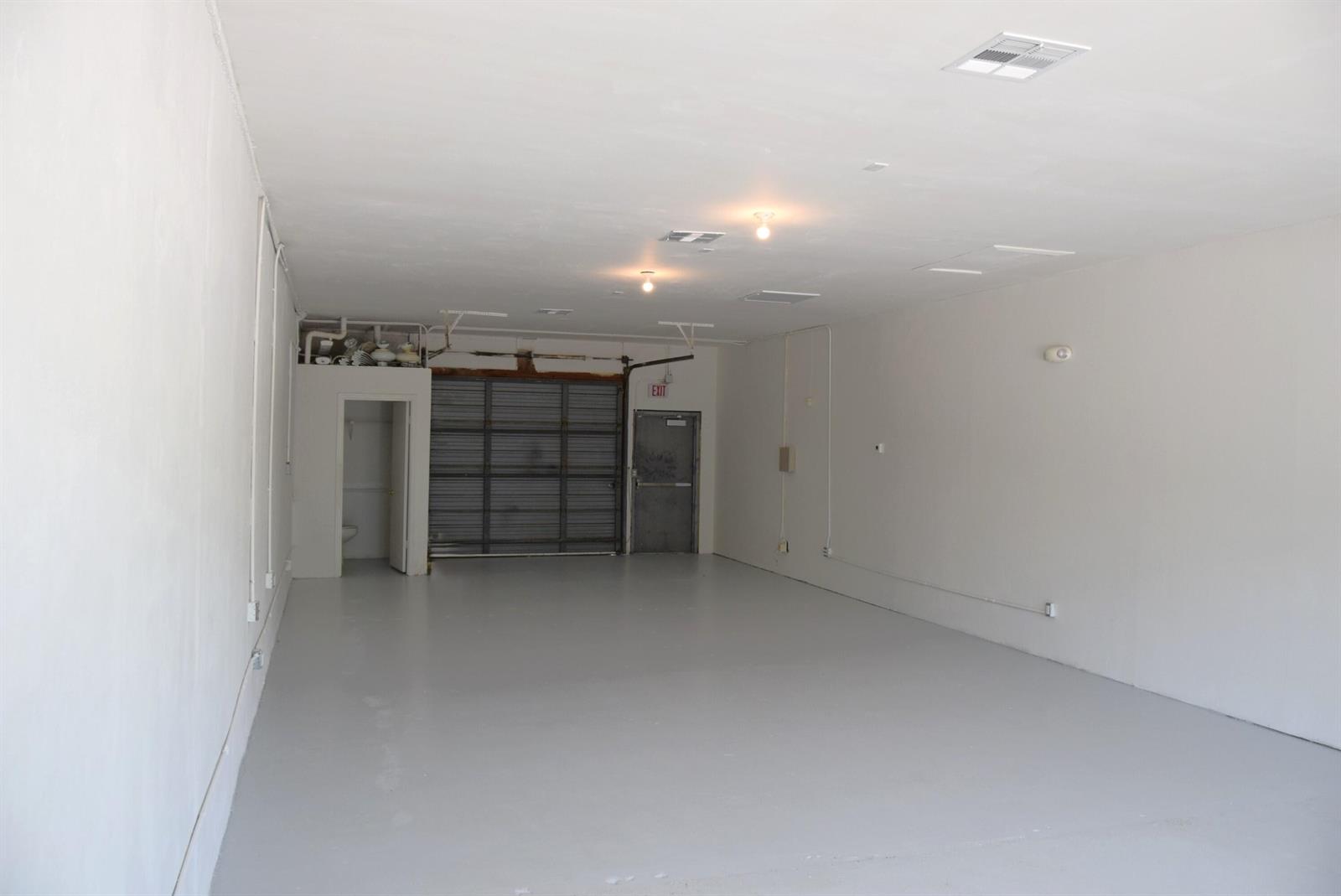 An empty, rectangular commercial space features white walls, a gray floor, and a rear garage door — 200 Hibiscus Street # 212, Jupiter FL 33458, JUPITER, FL