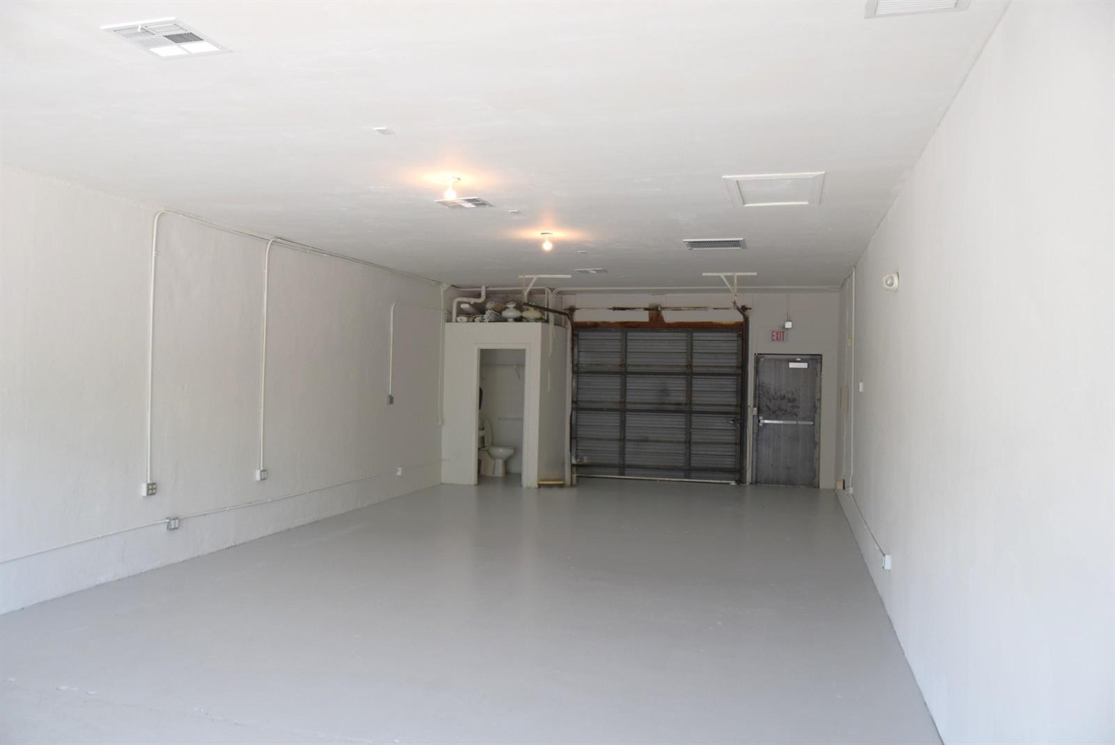 An empty commercial space with white walls, a gray floor, a roll-up door, and a restroom — 200 Hibiscus Street # 212, Jupiter FL 33458, JUPITER, FL