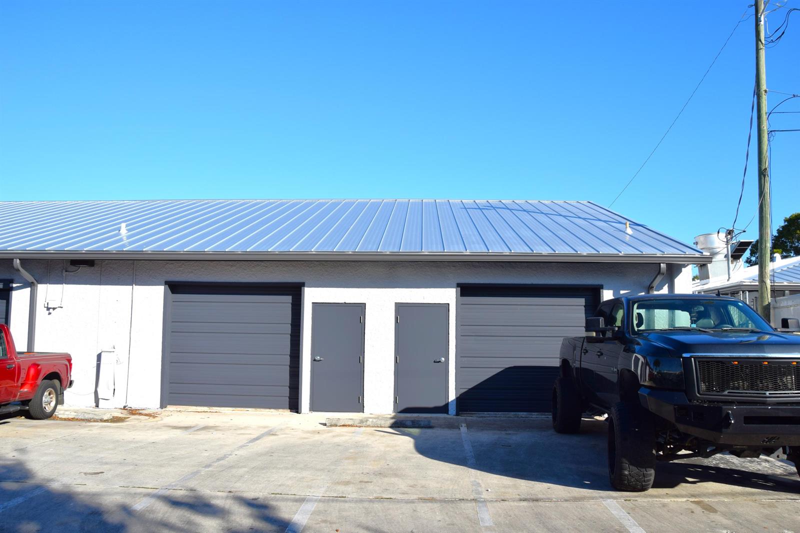 The exterior of a commercial building features two garage doors, two entry doors, and metal roofing — 200 Hibiscus Street # 212, Jupiter FL 33458, JUPITER, FL