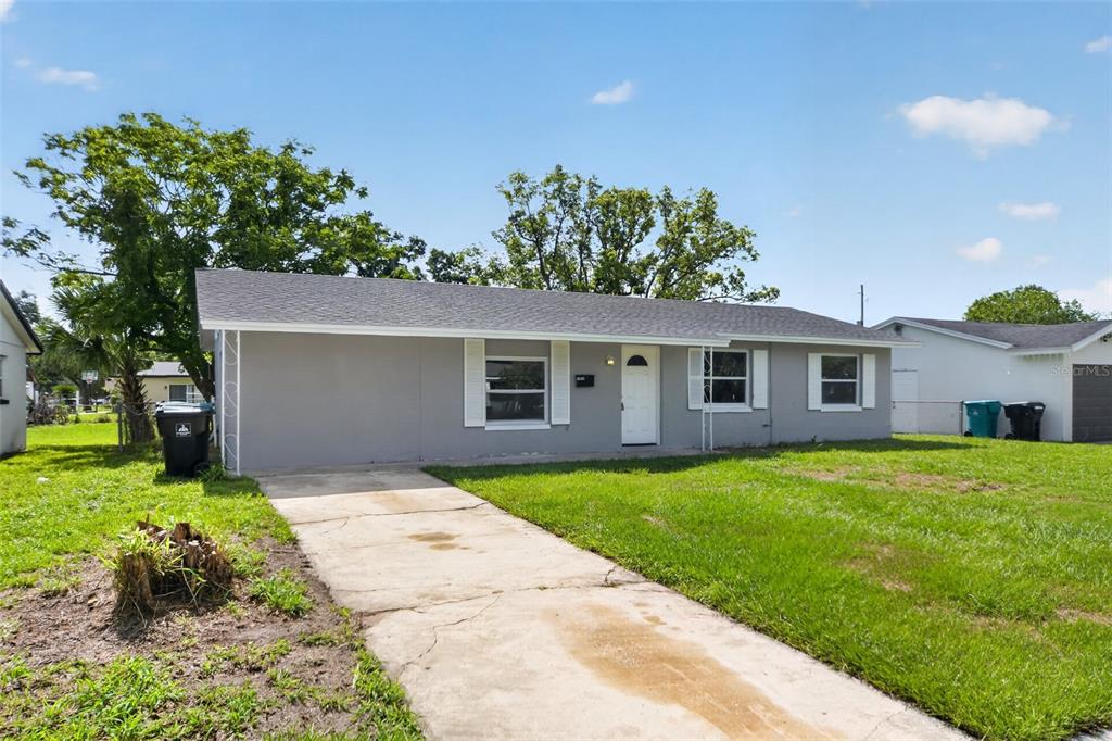 A single-story gray house with a concrete driveway and white shutters sits on a lawn — 1635 RAVENALL AVENUE, ORLANDO, FL
