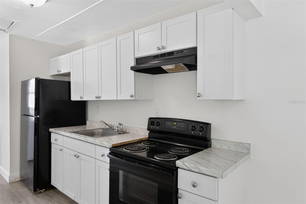 A kitchen features white cabinets, black appliances, and marble-patterned countertops — 1635 RAVENALL AVENUE, ORLANDO, FL