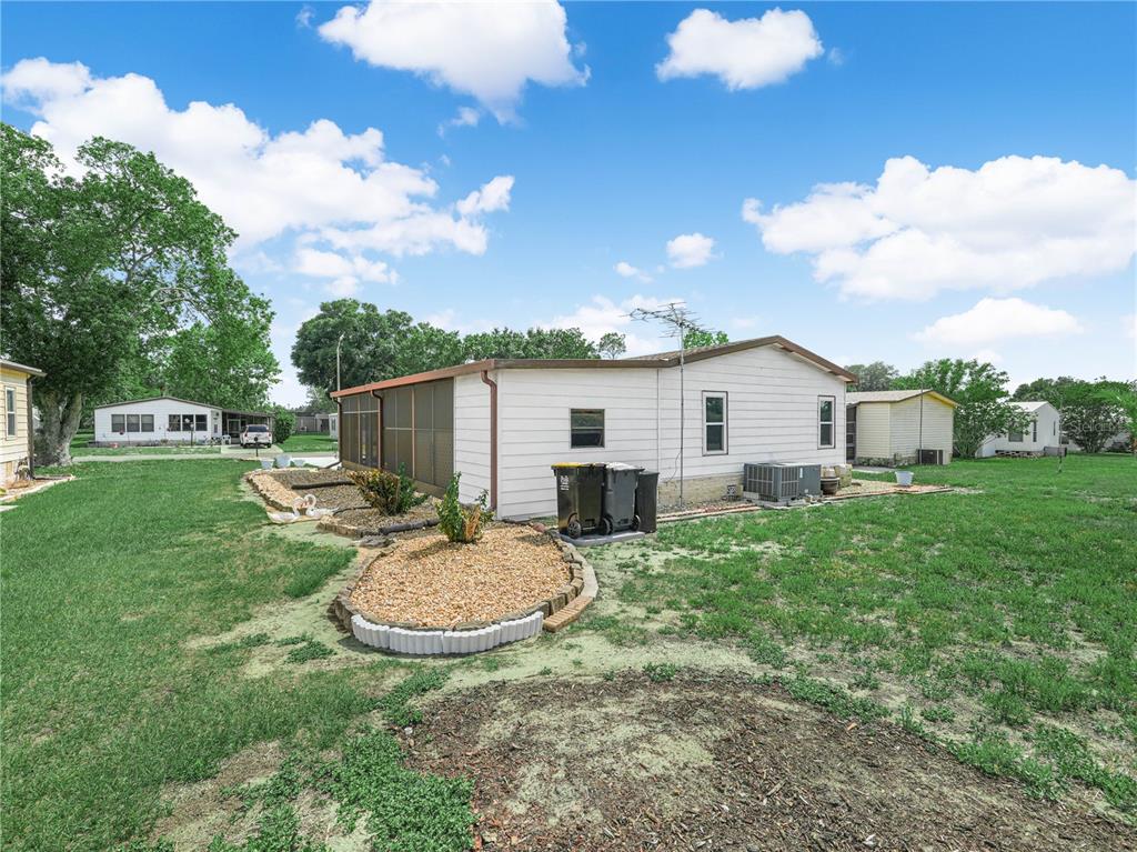 The exterior of a white mobile home features a screened-in porch and gravel landscaping beds — 124 KENSINGTON PARK DRIVE, DAVENPORT, FL