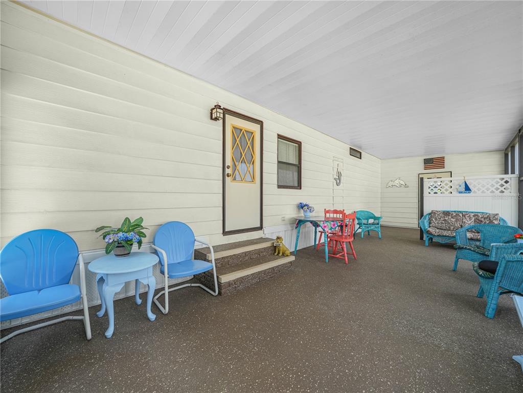 A covered outdoor patio features light-colored siding, blue metal chairs, and a small dining set — 124 KENSINGTON PARK DRIVE, DAVENPORT, FL
