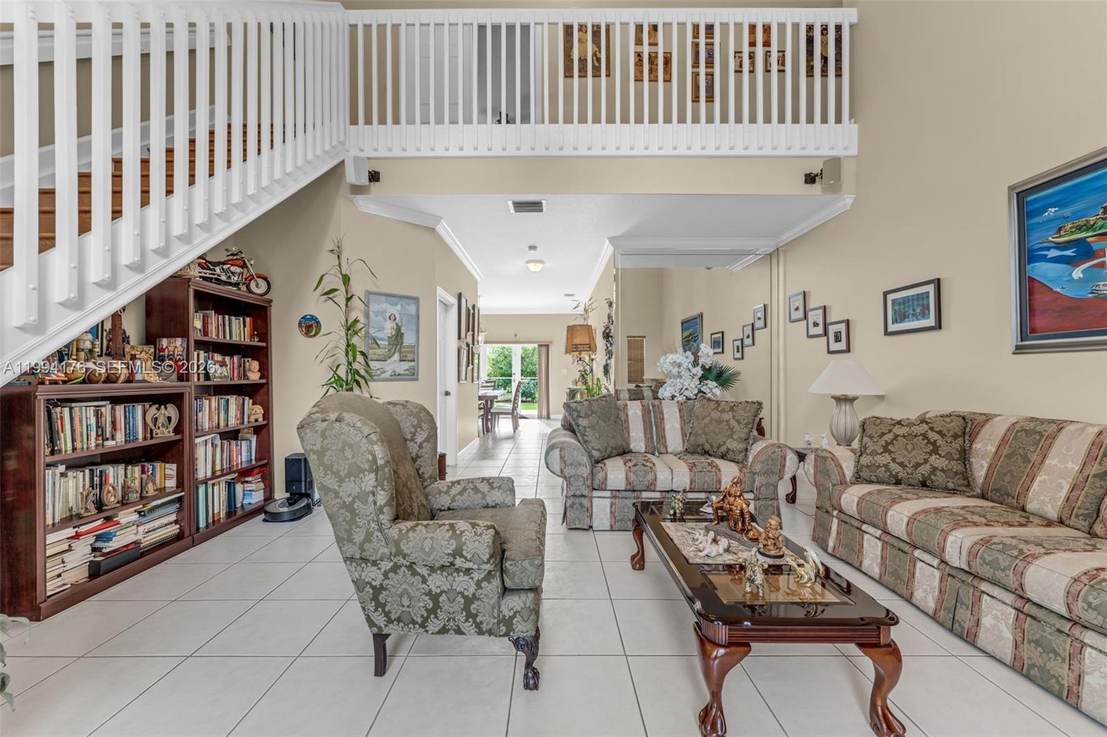A living room with a staircase, bookshelf, patterned furniture, and tile flooring — 6502 SW 157th Ct, Miami FL 33193, MIAMI, FL