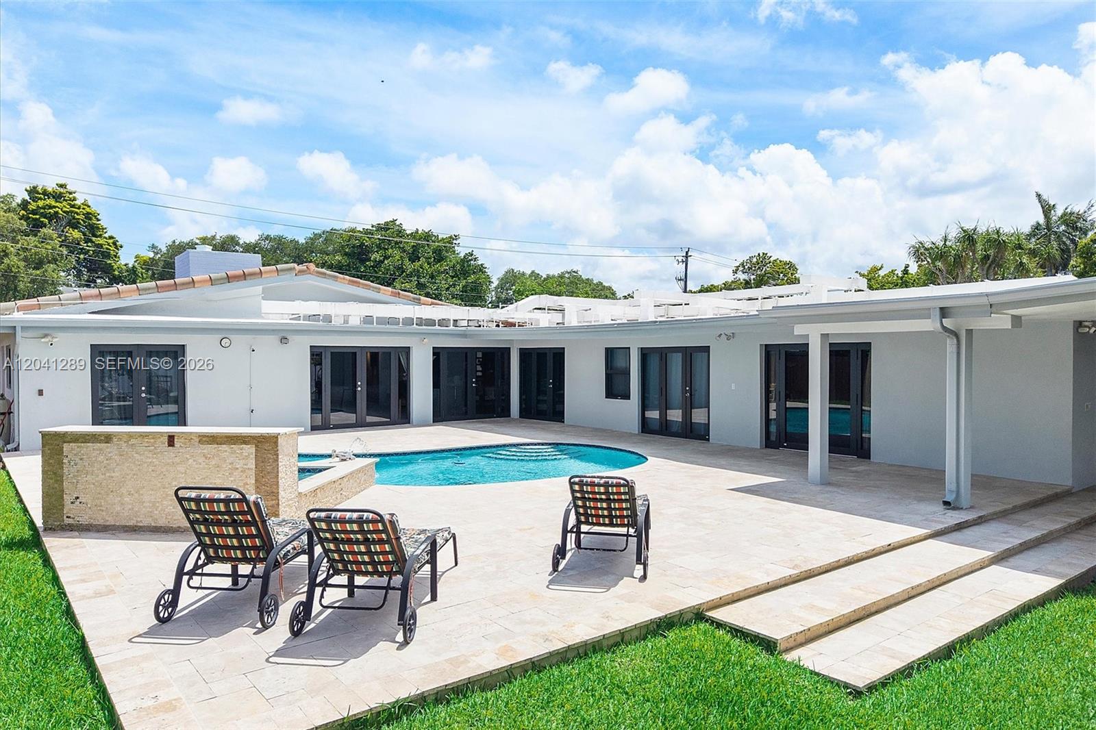 A backyard features a swimming pool, stone patio, lounge chairs, and a single-story house — 2531 NE 195th St, Miami FL 33180, MIAMI, FL