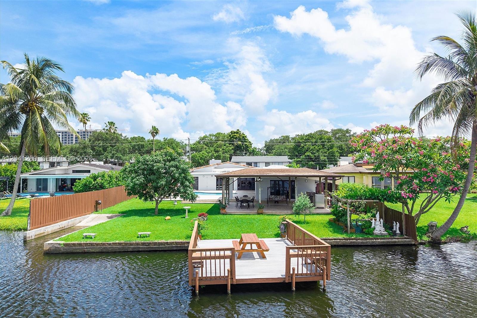 A waterfront backyard features a wooden dock, a covered patio, and a grassy lawn — 2531 NE 195th St, Miami FL 33180, MIAMI, FL