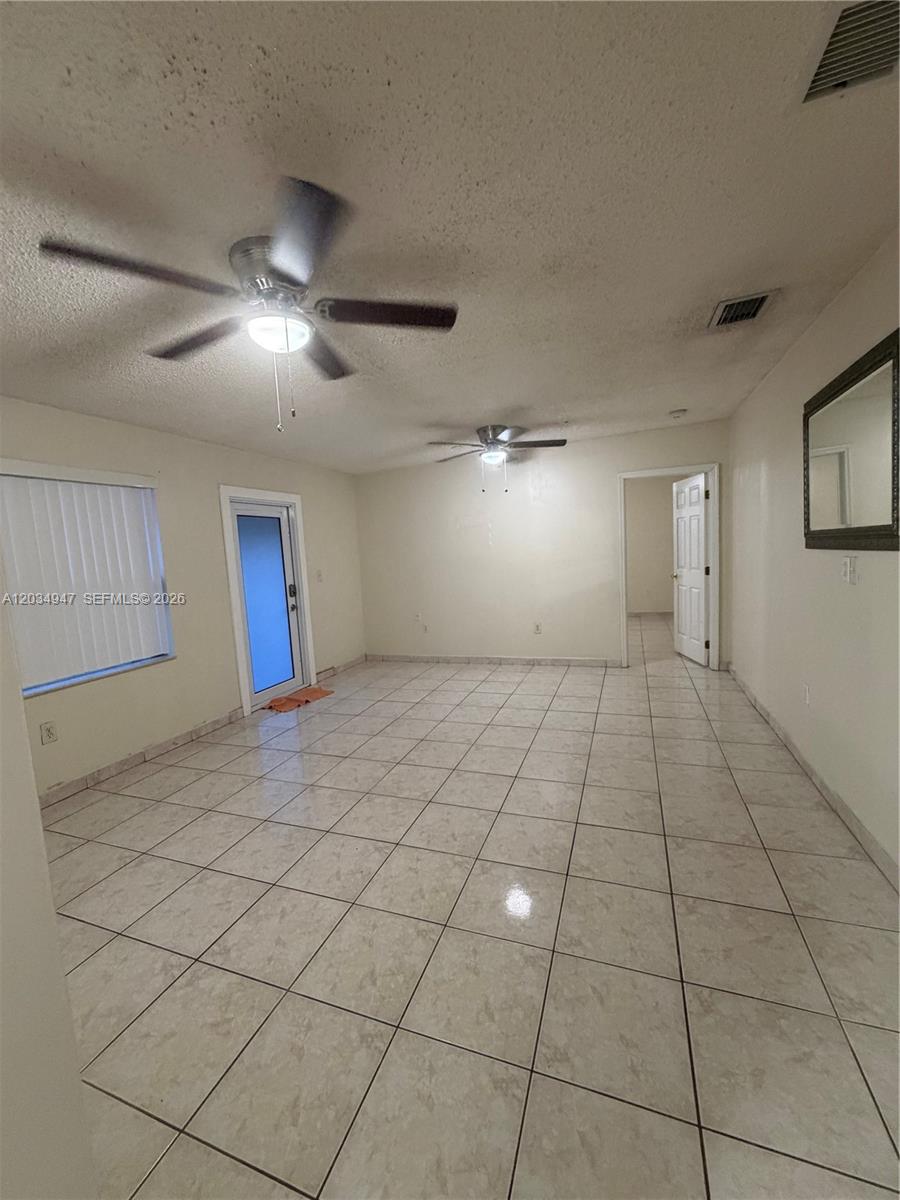 An empty room features light-colored tile flooring, two ceiling fans, and a glass-paneled door — 15431 SW 101st Ave, Miami FL 33157, MIAMI, FL
