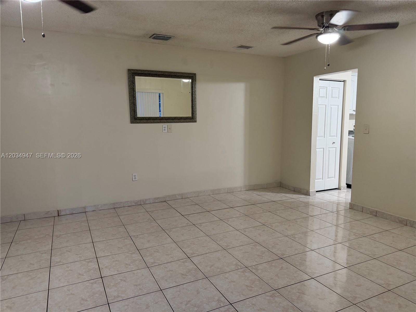 An empty room features beige tiled floors, a ceiling fan, and a wall-mounted mirror — 15431 SW 101st Ave, Miami FL 33157, MIAMI, FL