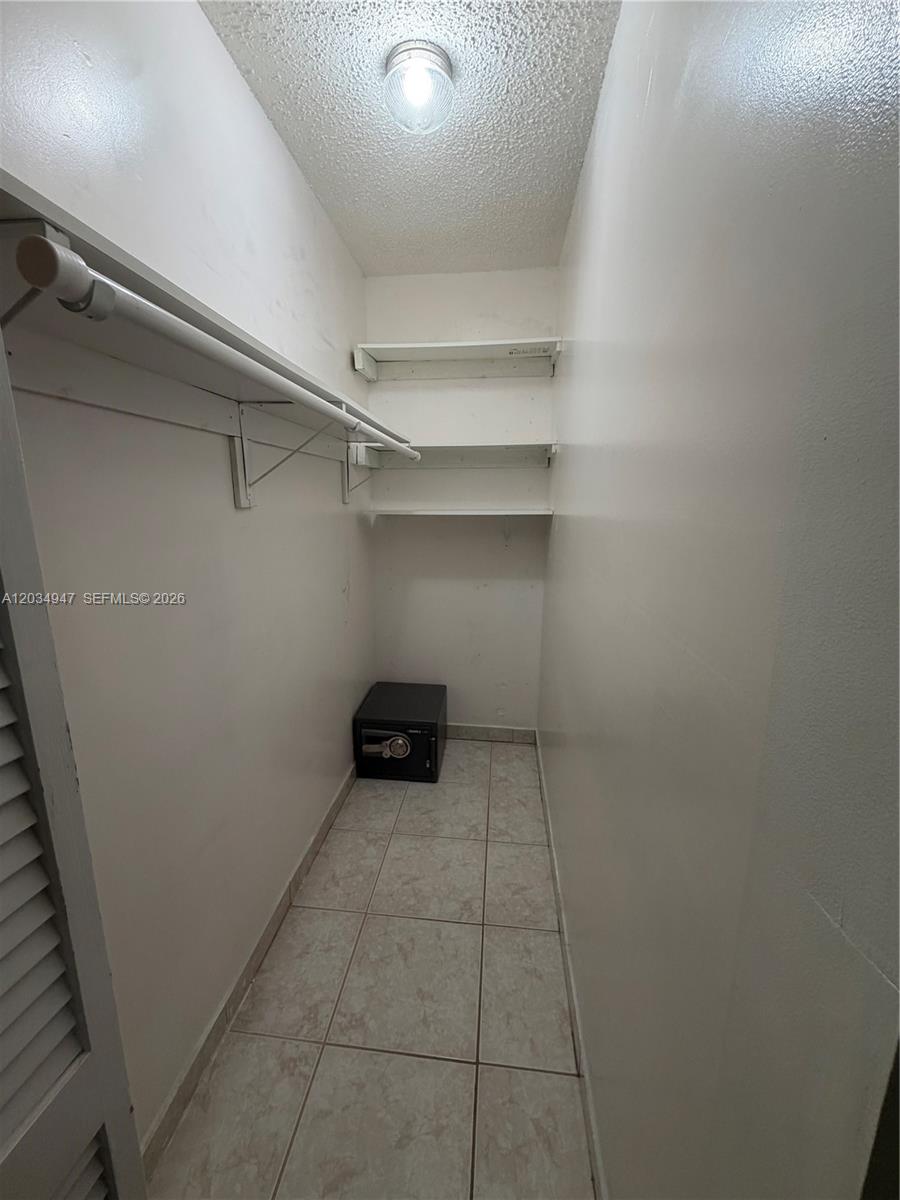 A small walk-in closet features white walls, tile flooring, a hanging rod, shelves, and a safe — 15431 SW 101st Ave, Miami FL 33157, MIAMI, FL