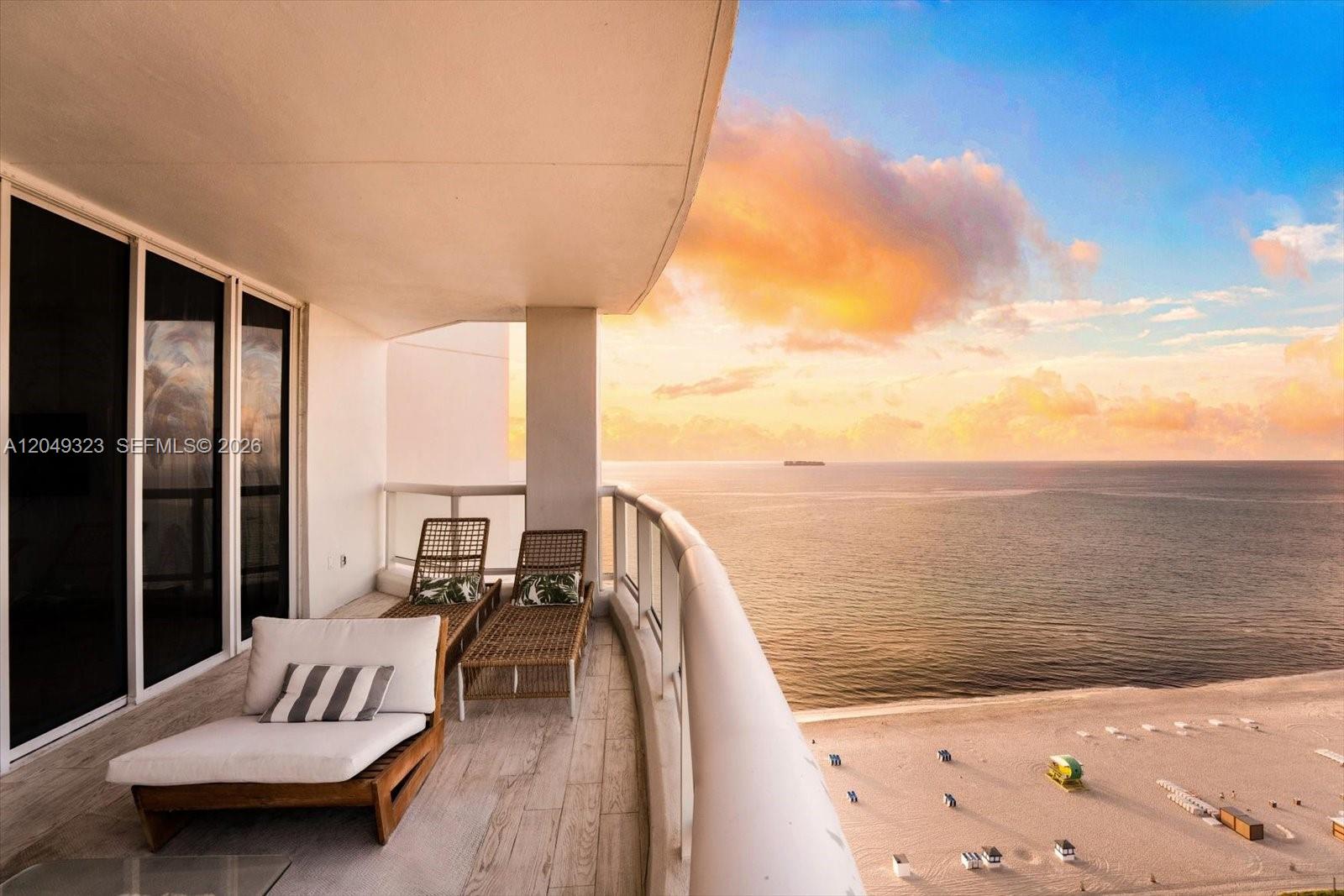 A balcony with lounge chairs overlooks a sandy beach and the ocean at sunset — 4201 Collins Ave # 2301, Miami Beach FL 33140, MIAMI BEACH, FL