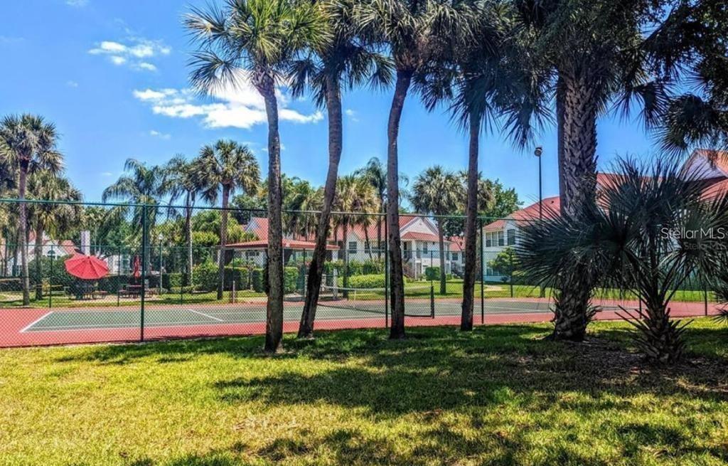 A tennis court is surrounded by a chain-link fence and palm trees near residential buildings — 11526 WESTWOOD BOULEVARD UNIT 717, ORLANDO, FL