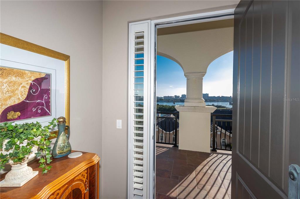 An open door reveals a balcony with a stone pillar overlooking a water view — 202 WINDWARD PASSAGE UNIT 603, CLEARWATER BEACH, FL