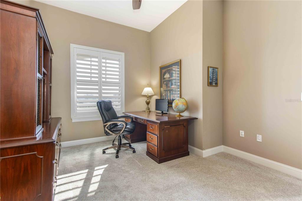 A home office features a wooden desk, a black leather chair, and a window with shutters — 202 WINDWARD PASSAGE UNIT 603, CLEARWATER BEACH, FL