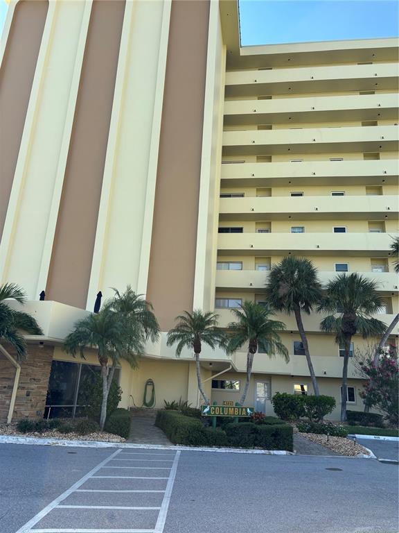 A multi-story yellow apartment building features a ground-level entrance with palm trees and landscaping — 4725 COVE CIRCLE UNIT 104, ST PETERSBURG, FL