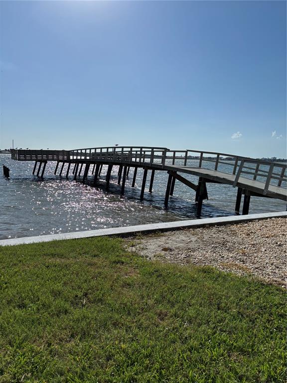 A wooden pier extends into the water from a grassy shoreline under a clear sky — 4725 COVE CIRCLE UNIT 104, ST PETERSBURG, FL